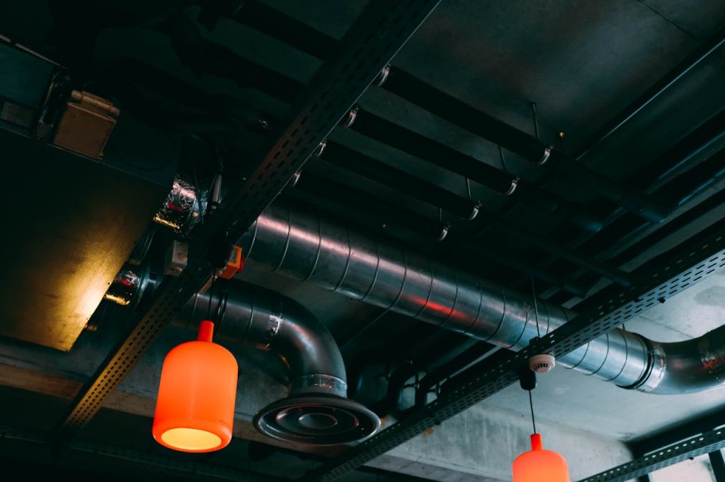 gray-rod-and-pendant-lamps-on-ceiling-2464420 Low-angle view of a modern industrial ceiling featuring ducts and red lamps.